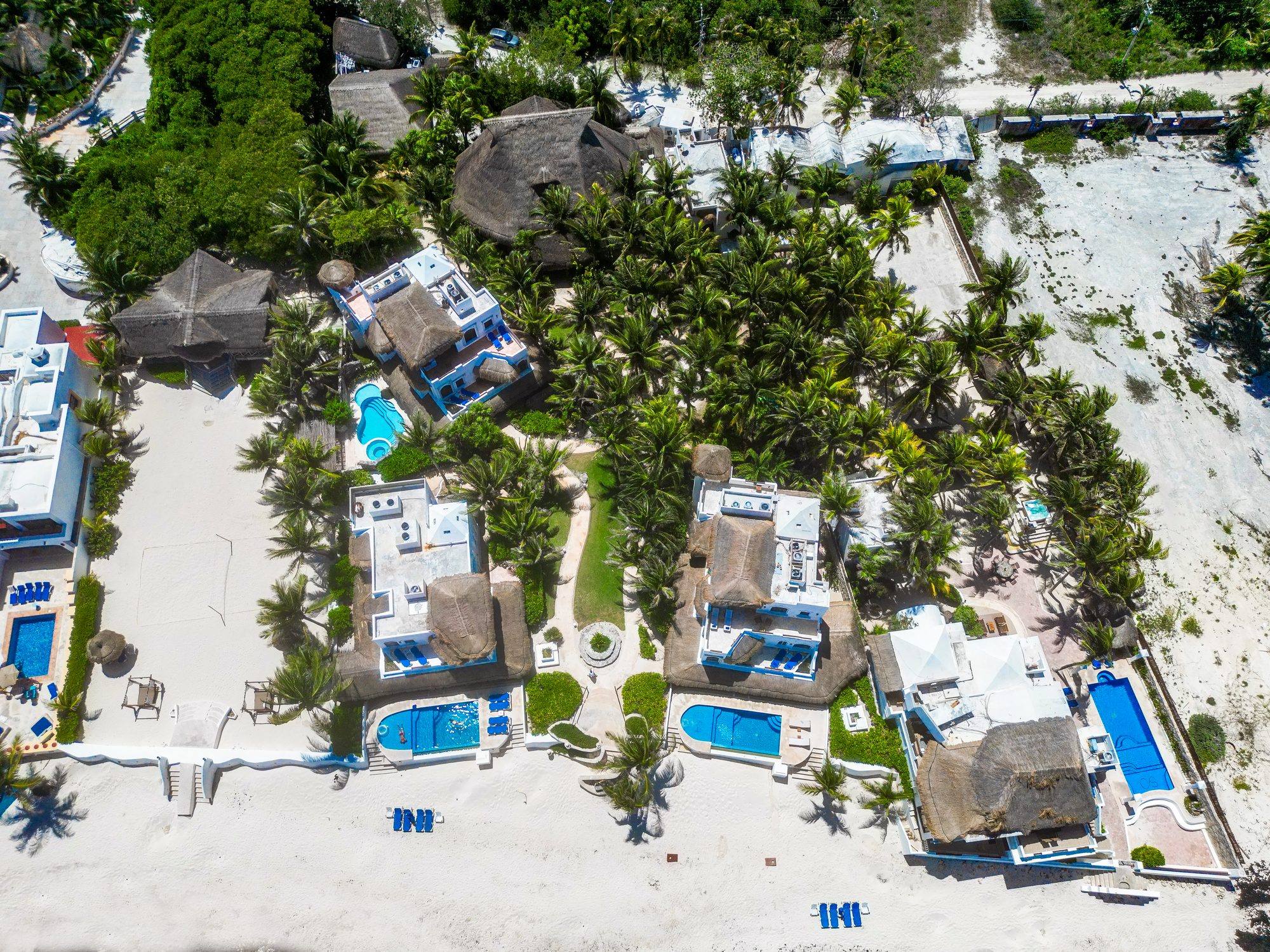 The whole estate from directly above — villas and pools around shared gardens with the beach below