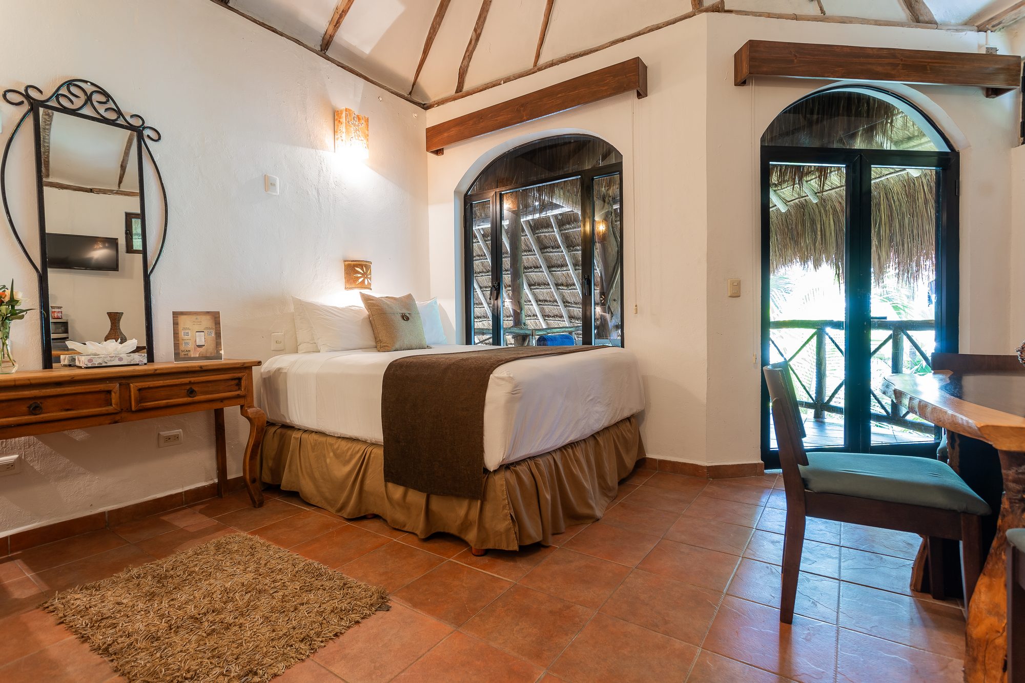 A queen bedroom in the Palapa Family Suite with arched doors onto the thatched balcony