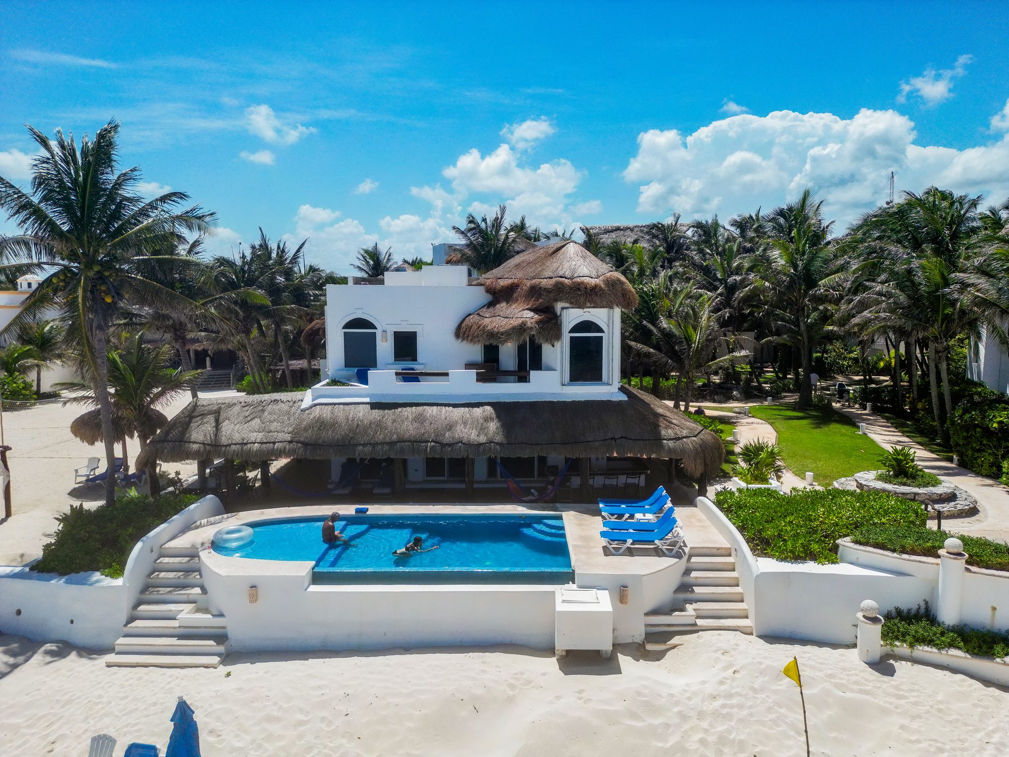 An estate villa with a grand palapa roof and oval pool at the edge of the sand