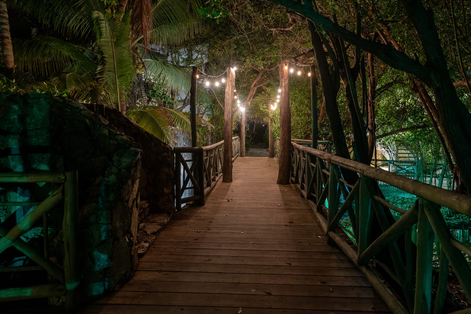 The estate's string-lit wooden bridge crossing through the gardens at night