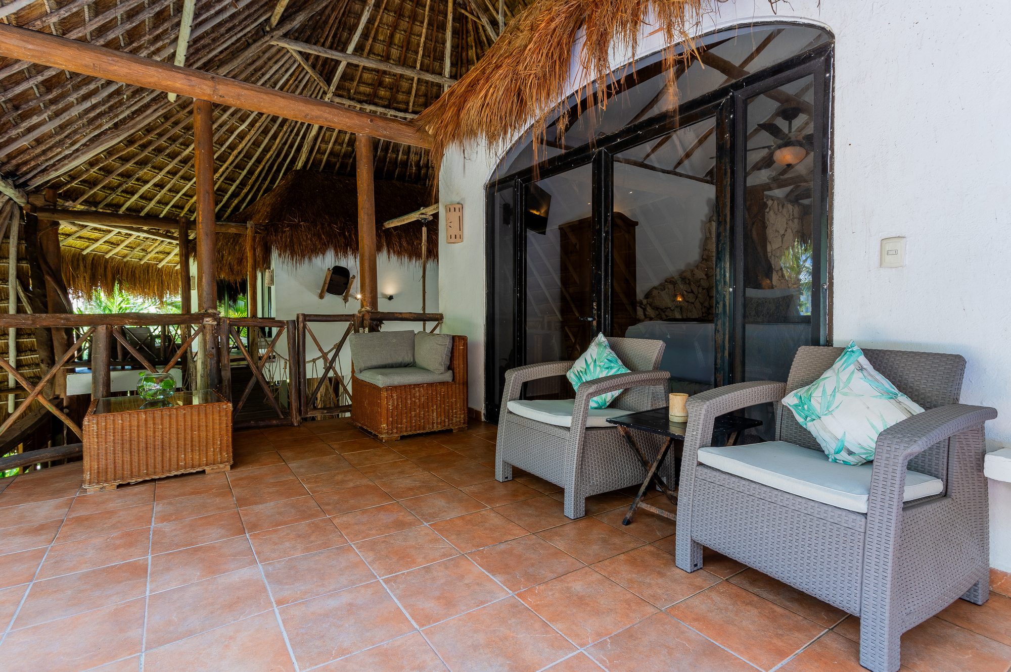 The covered terrace lounge under the palapa roof outside the suite's arched glass doors