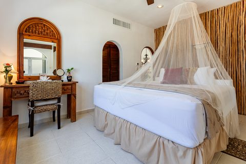 A king bed under a sheer canopy net against a bamboo-pole feature wall in Villa Canteena