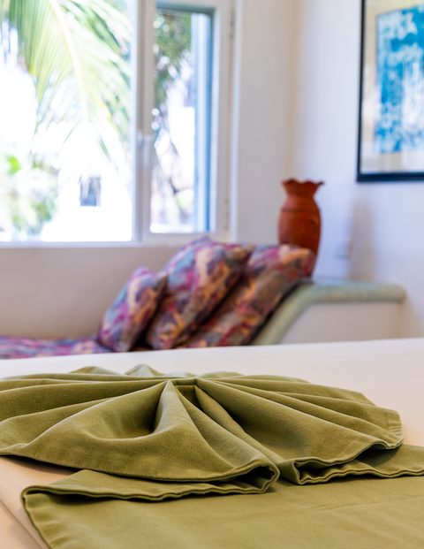 A fan-folded green throw at the foot of a made bed in Villa Sarita