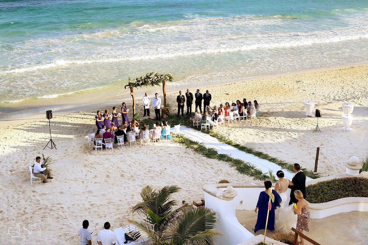 Aerial view of a beach wedding ceremony set on the sand at Hacienda del Secreto, with a floral arch, white chairs and a palm-lined aisle by the Caribbean