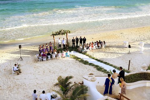Aerial view of a beach wedding ceremony set on the sand at Hacienda del Secreto, with a floral arch, white chairs and a palm-lined aisle by the Caribbean