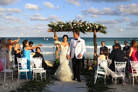 Newlyweds walk back down the sand aisle through a shower of petals after their beach ceremony